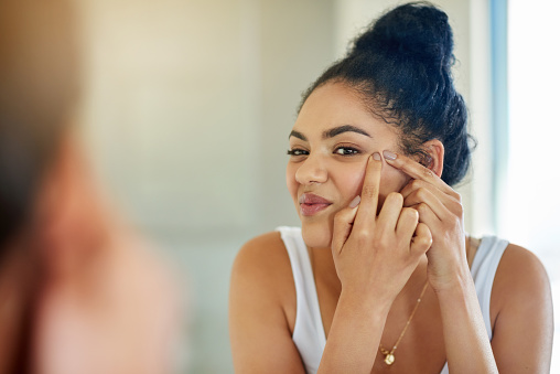 Shot of a young woman squeezing a pimple in front of the bathroom mirror